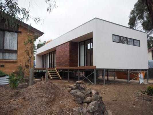 White flat design with wooden floors and stairs, glass doors and windows. Located on top of constructed steels.